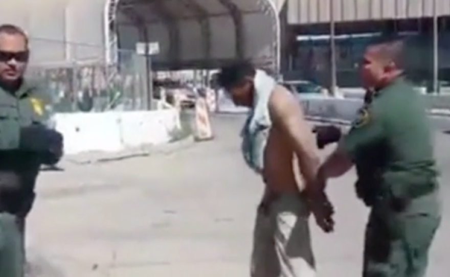 A screenshot of a video showing U.S. border patrol agents attempting to instruct an injured man to cross the U.S. border into Mexico, apparently violating international laws.