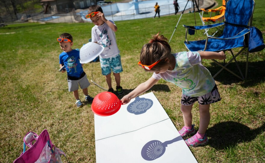 Maeve Beebe (right), 4, of Auburn, Mich., makes crescent-shaped shadows with a colander alongside her cousin, Gavin Stodolak (far left), 3, of South Lyon, Mich., and her brother, Everett, 7, at Cole Memorial Park in Chester, Ill.