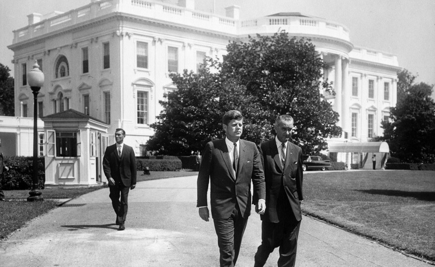 President John F. Kennedy and Vice President Lyndon B. Johnson walk across the South Lawn of the White House in Washington, D.C. to attend a ceremony marking the fiftieth anniversary of the first state Workmen's Compensation Law, enacted in Wisconsin in 1911, on the South Lawn. Secret Service Agent Bob Lilley follows. Aug. 31, 1961.