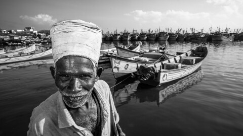 Pavadairayan, 60, a migrant laborer known as a "basket man," carries fish in a basket on his head from boats to the auction house at Kasimedu Fishing Harbour in Chennai, India.