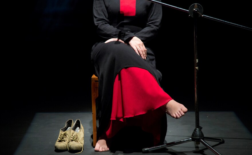 During the last rehearsal before opening night, a Syrian Palestinian refugee recounts onstage the day she went back to her house in the Yarmouk camp in Syria after it was bombed. The shoes beside her are the ones she was wearing that day she entered the camp.