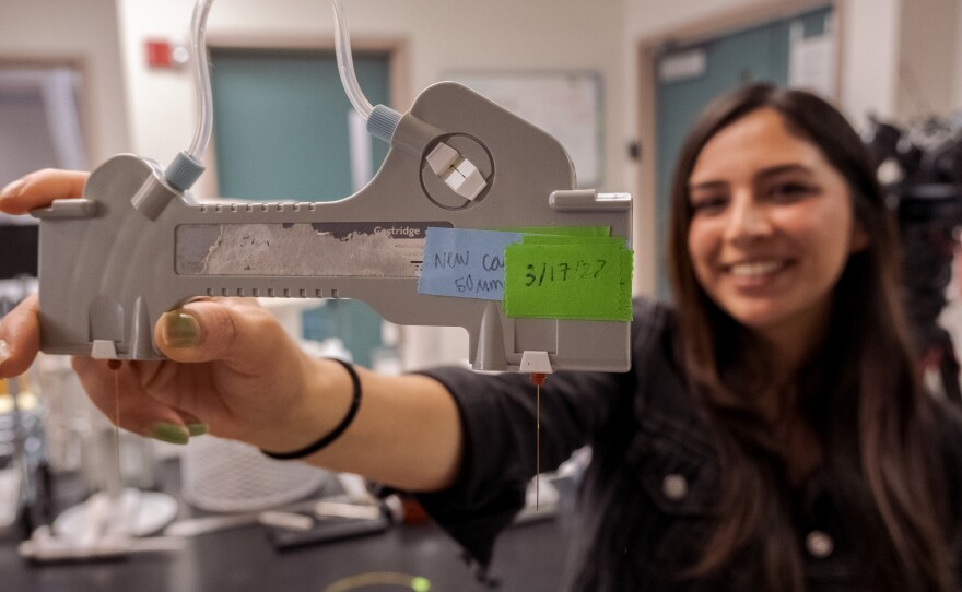 In the chemistry lab, Jessica Torres holds up a device that tests molecules that run though a tiny glass tube that's mounted inside it. April 5, 2022.