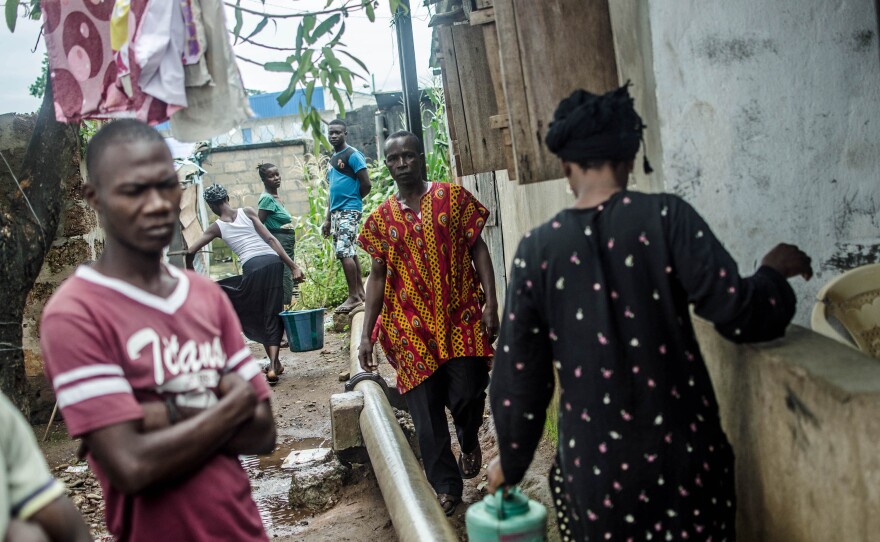 Saudatu Koroma's mother, Hana Conteh (right), leaves the quarantined house to collect water, while her father Mohamed Koroma (in red) returns.