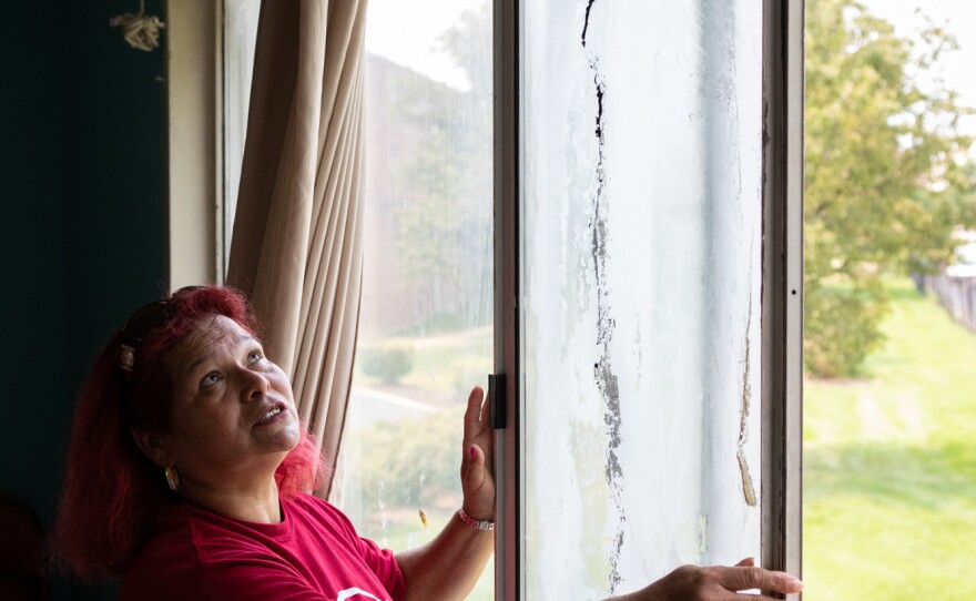 María Lara shows a loose and broken window in her home. She says she is afraid it will fall and hurt her daughter.