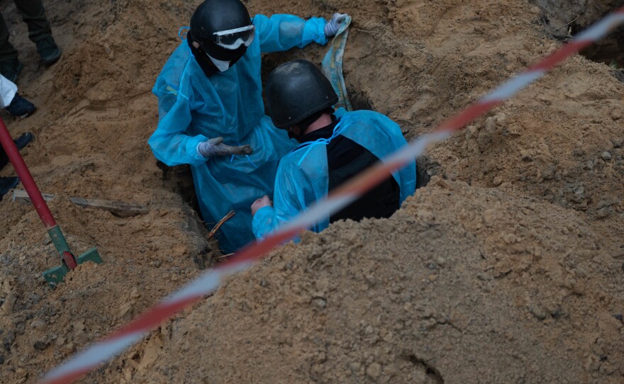 Ukrainian investigators exhume bodies from a mass grave site in Izium on Friday.