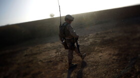 A Marine walks along a  mud wall while conducting a search and clearing operation in Afghanistan's Helmand province, as the dust from a wheat thrashing machine falls like snow.