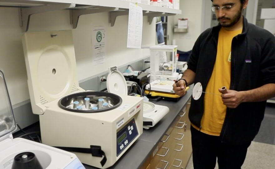 Saad Bhamla holds the paperfuge next to an electrical centrifuge. Both can separate blood samples.