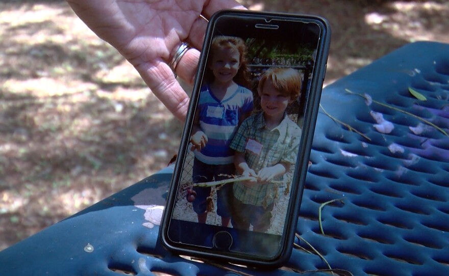 Rusti Dixon holding a phone showing her children, Carson and Addison, when they were younger standing in the Children's Garden at Alta Vista Botanical Gardens, Aug. 20, 2024.