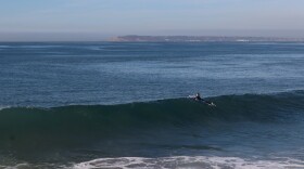 A surfer floats along the top of a wave at Imperial Beach on Monday, Dec. 2, 2024.