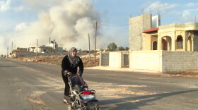 Moments after a deadly air strike hits the Sunni village of Al Barra, a Syrian woman pushes her stroller away from the blast.