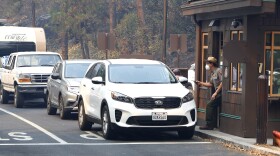 Park Ranger Alex Martinez passes maps out and directs visitors at the Hwy 140 gate as Yosemite National Park reopens after a three week closure from smoke and fires that led to most tourists canceling their trips Tuesday, Aug. 14, 2018 in Yosemite, Calif. 
