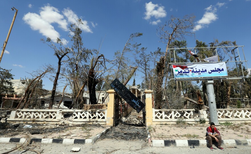 A Syrian youth sits outside the destroyed municipality building on Thursday in the modern town of Palmyra, adjacent to the ancient Syrian city. Syrian media report a mass grave with about 40 bodies was discovered in a northeastern neighborhood of the town.