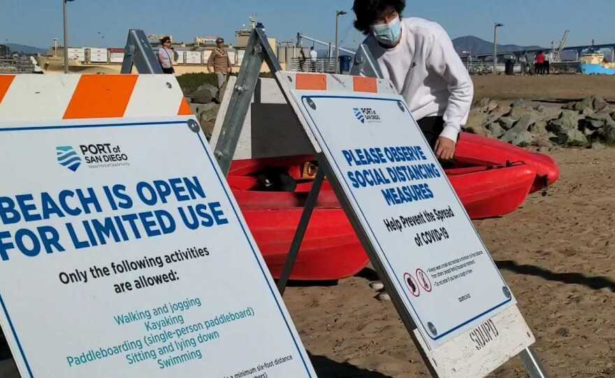 A kayaker getting ready to put away kayaks as the sign at Coronado Ferry Landing reads "Beach Is Open For Limited Use," because of the coronavirus pandemic, Feb. 21, 201