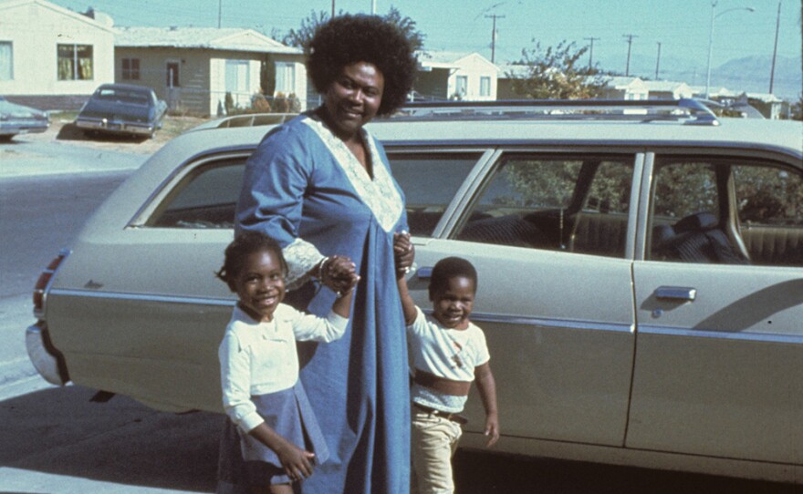 
 Ruby Duncan holds the hands of two children on a sunny driveway.