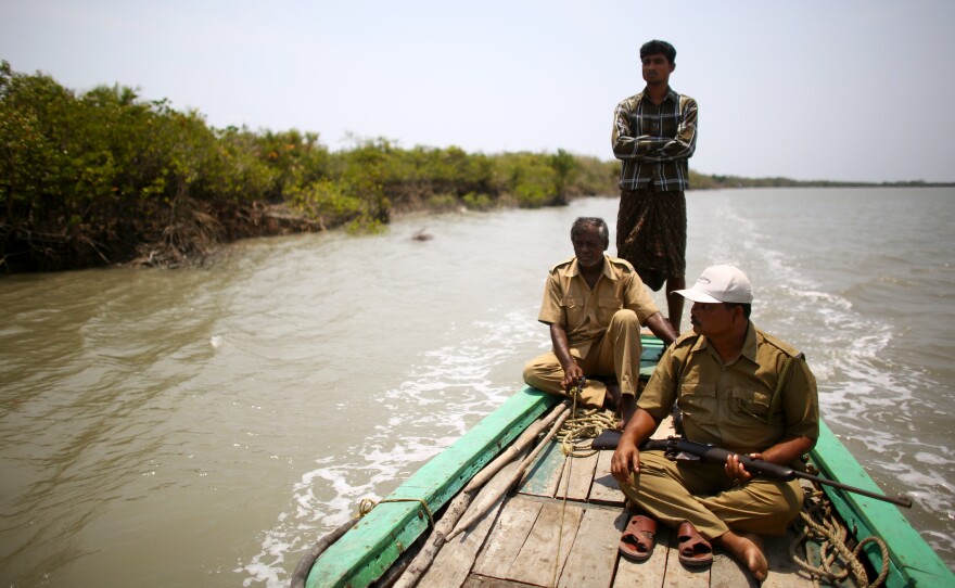 Debnath Mondal (front right), who survived a tiger attack in 2010, patrols the banks of the Sundarbans tiger preserve with another forest guard and a boat skipper.