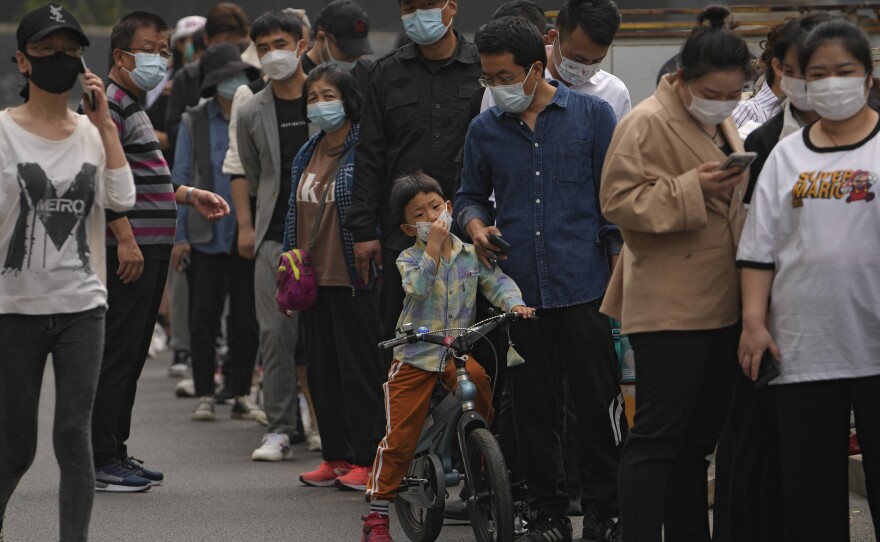 Residents and office workers wearing face masks line up for mass coronavirus testing outside a commercial office complex in Chaoyang district on Monday in Beijing.