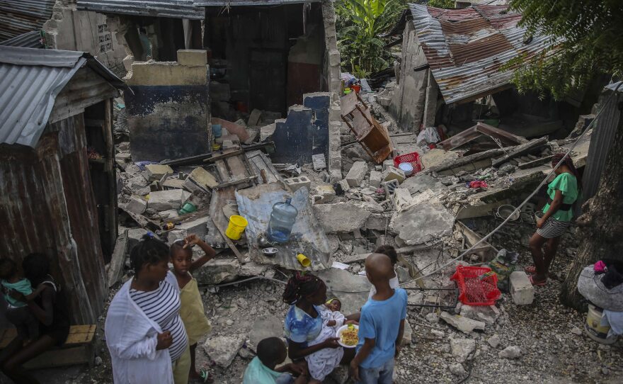 <strong>Sun., Aug. 15:</strong> A family eats breakfast in front of homes destroyed the earthquake in Les Cayes.