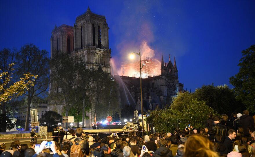 Crowds watch as flames and smoke billow from the cathedral's roof.