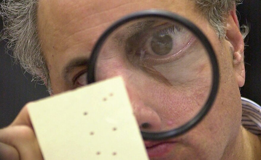 Broward County, Fla., canvassing board member Judge Robert Rosenberg uses a magnifying glass to examine a disputed ballot on Nov. 24, 2000.