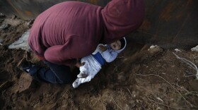 A Honduran migrant passes his eight-month-old son through a hole under the U.S. border wall to his partner who had already crossed, in Tijuana, Mexico, Friday, Dec. 7, 2018. 