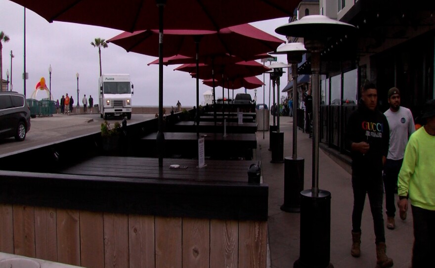 People walk by a dining area in Mission Beach that extends to the street parking.