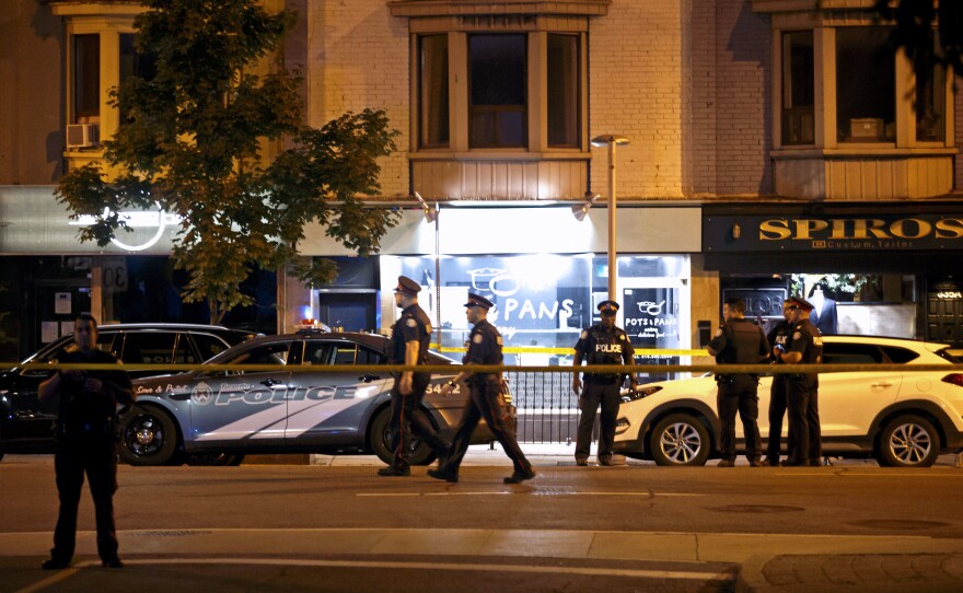 Police officers walk the scene in the Greektown neighborhood of Toronto Sunday night. Police say a gunman opened fire on 14 people in a restaurant. Three people are dead including the gunman, police reported.