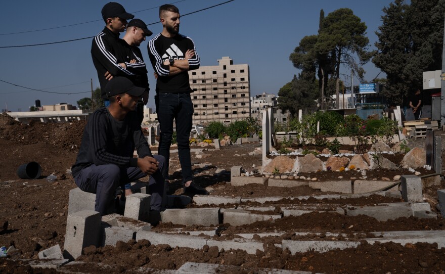 Young men stand in front of recently dug graves of people killed by Israeli forces in Jenin. More than 100 Palestinians have been killed in the West Bank in the three weeks since the war began.