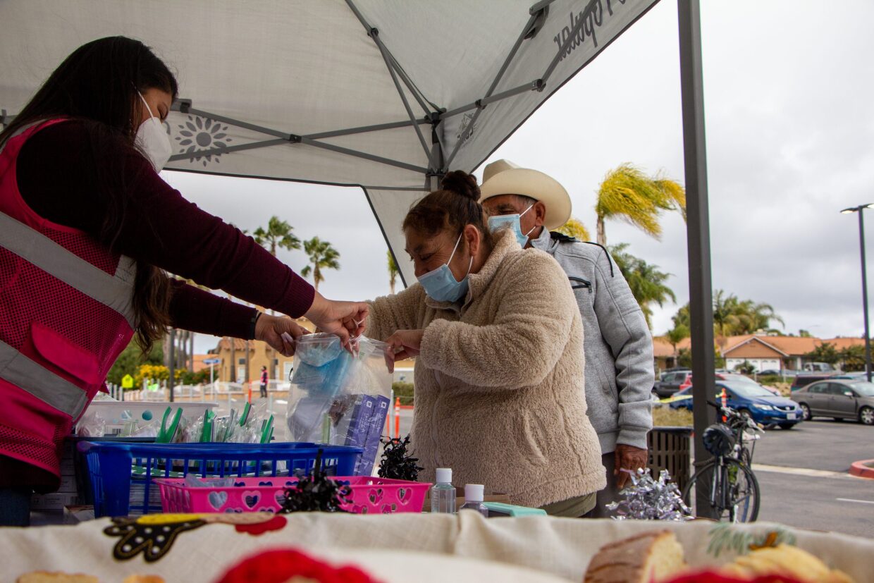 Lilian Serrano helps Maria Roja bag face masks and rapid COVID-19 tests outside of a vaccine clinic at La Mirada Academy in San Marcos, Calif. in this undated photo.