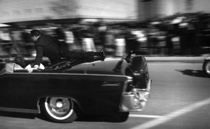The limousine carrying President John F. Kennedy races toward the hospital after he was shot in Dallas on Nov. 22, 1963, with Secret Service agent Clinton Hill riding on the back.