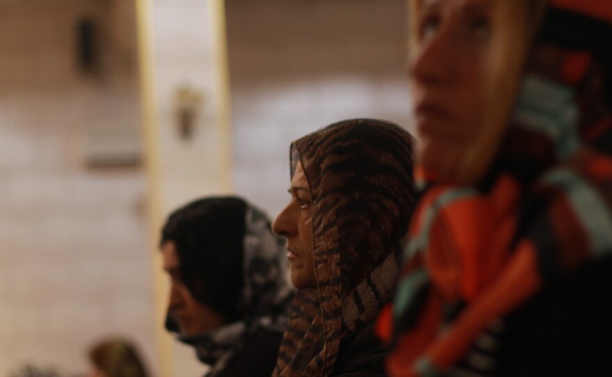 Women at a service in the Church of Our Lady in northern Syria. The women sit at the back, and cover their heads with scarves — a selection of colorful headscarves are kept at the back of the church.