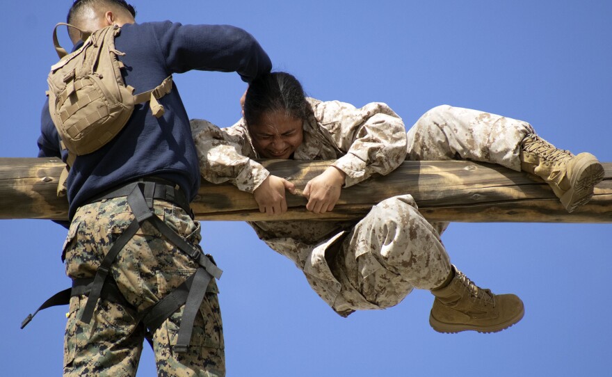 A Marine recruit climbs over a wooden obstacle during the confidence course, March 9, 2021.