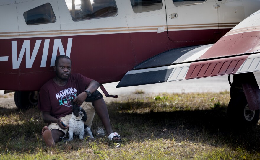 Evacuee Samazio Rolle and his dog, Logan, sit in the shade next to an airplane in the afternoon heat at a landing strip on Abaco, in hopes of catching a flight to Nassau. The pair survived Hurricane Dorian's punishing strike on the Bahamas — and now they want to leave Abaco.