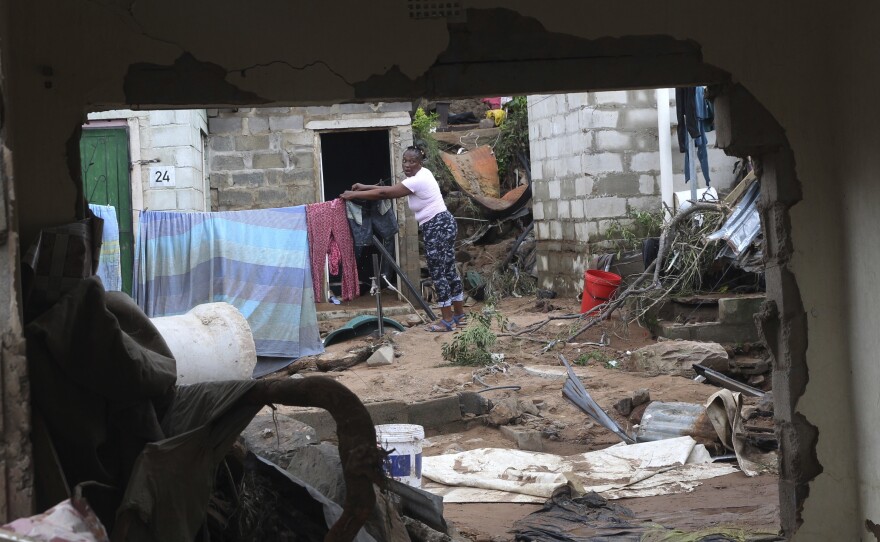 A woman is seen through a damaged wall hanging her clothes on a makeshift washing line in Ntuzuma, outside of Durban, South Africa, on Wednesday. Flooding in South Africa's Durban area has taken killed at least 259.