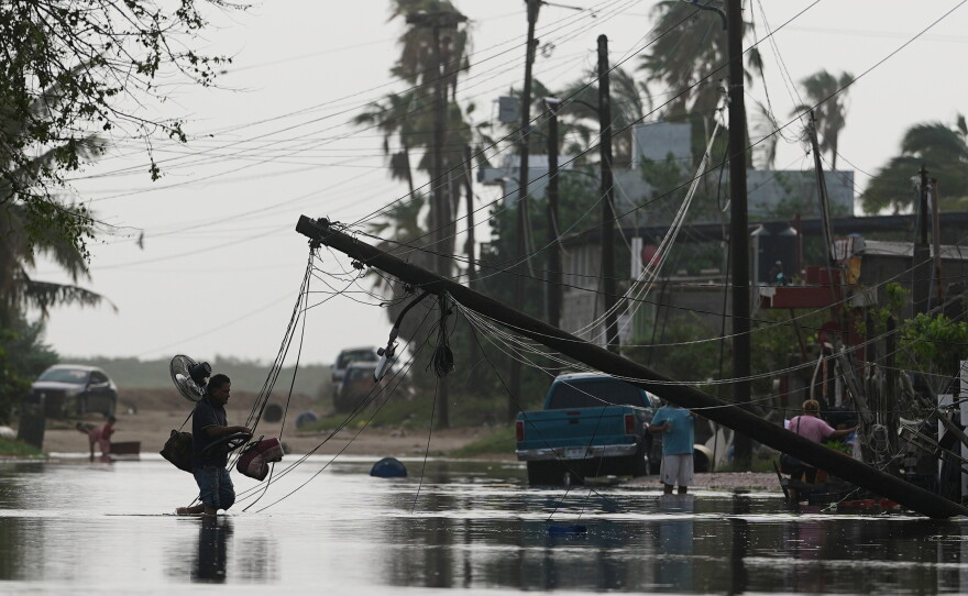 A man carries items through floodwater past downed electric lines after the passing of Hurricane Polo in Puerto San Carlos, Baja California Sur state, Mexico, Tuesday, Sept. 29, 2026.