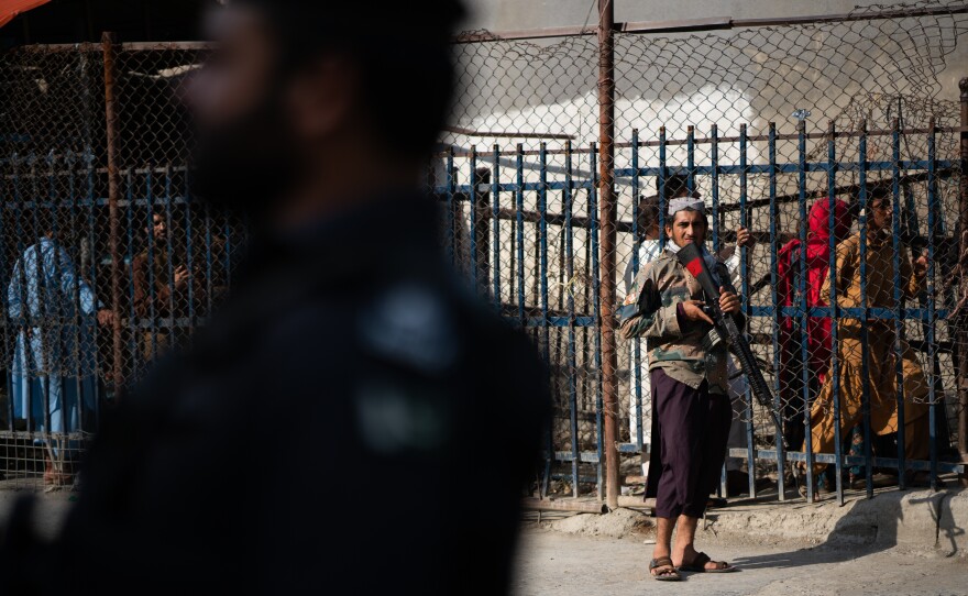 A Taliban guard stands on the Afghan side of the Torkham border crossing with Pakistan. People behind wait either to leave Afghanistan or to receive those returning to the country.