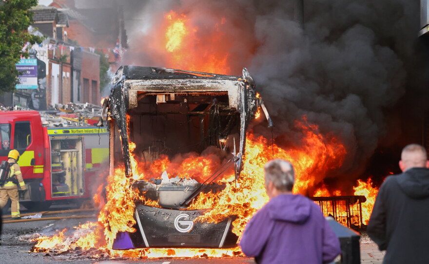 People watch as firemen arrive to put out vehicle that was set alight during a protest in East Belfast following a stabbing incident in Belfast, Tuesday, June 9, 2026.