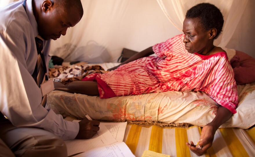 An HIV-positive woman, living alone in a one-room house, speaks with a visiting doctor.