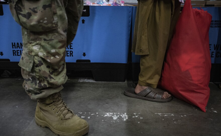 Standing in front of a soldier, a young Afghan refugee, who is partially blind, waits in line for new clothes at the military base.