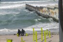 Two people sit on a bench watching waves crash along the border wall, March 14, 2024. Strong rip currents and heavy surf make swimming around the border wall dangerous. Tijuana lifeguards have rescued a record-number of migrants in recent years.