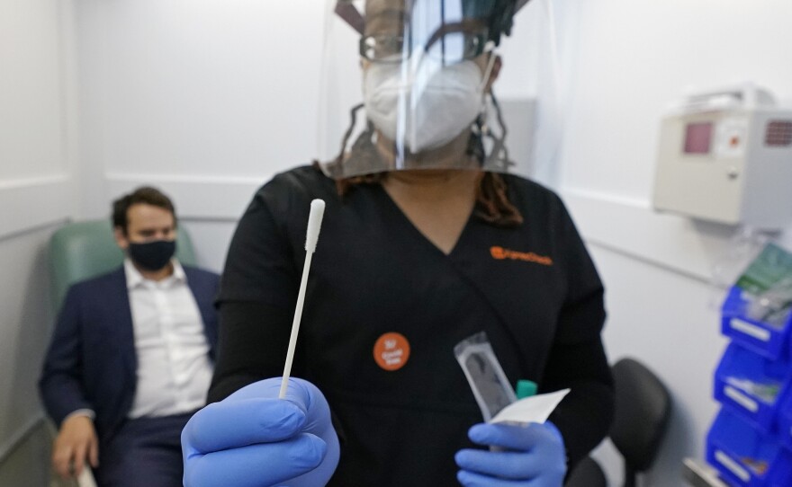 A medical assistant holds a swab after testing a man on Wednesday at the new COVID-19 testing facility at Boston Logan International Airport.