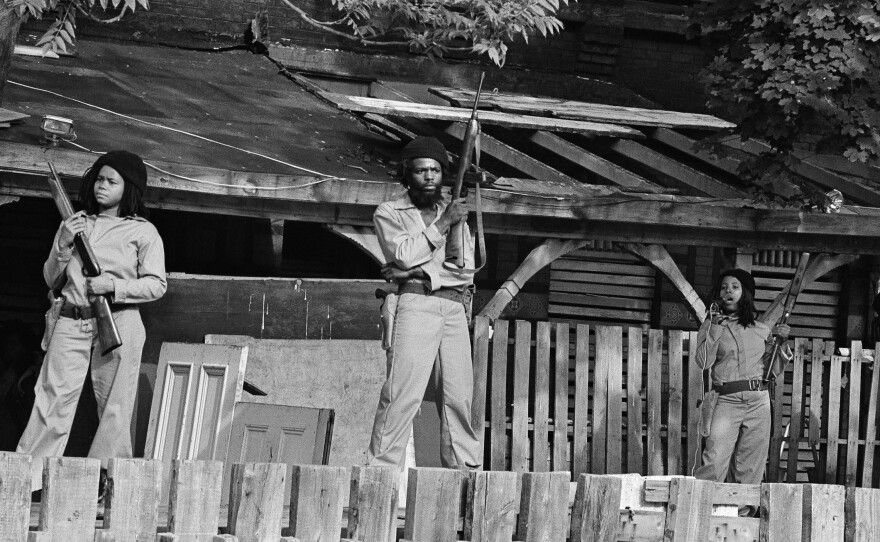 MOVE members hold sawed-off shotguns and automatic weapons as they stand in front of their barricaded headquarters on May 21, 1977.