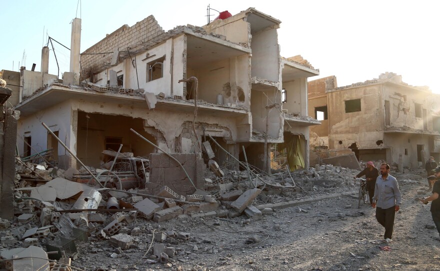 Syrians walk past a building destroyed in a reported air strike by government forces on the rebel-held town of Douma, northeast of the capital Damascus on June 16, 2015, allegedly by a barrel bomb dropped by the Syrian air force.