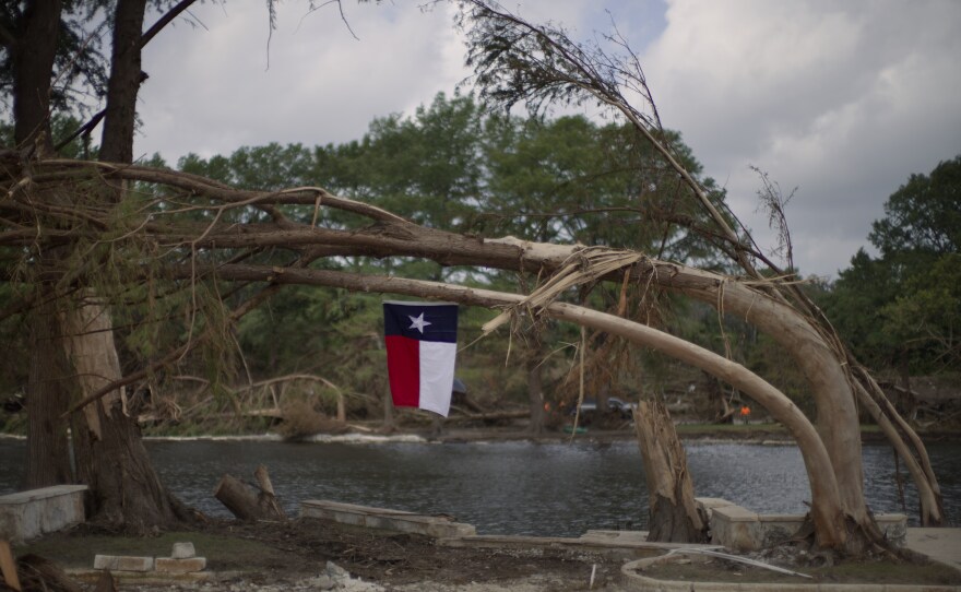 A Texas flag hangs from a flood-damaged tree on the bank of the Guadalupe River in Kerrville, Texas after deadly floods in July 2025. A group of emergency experts appointed by President Trump is recommending that the Federal Emergency Management Agency (FEMA) provide less money to states to help prepare for and respond to disasters including floods.
