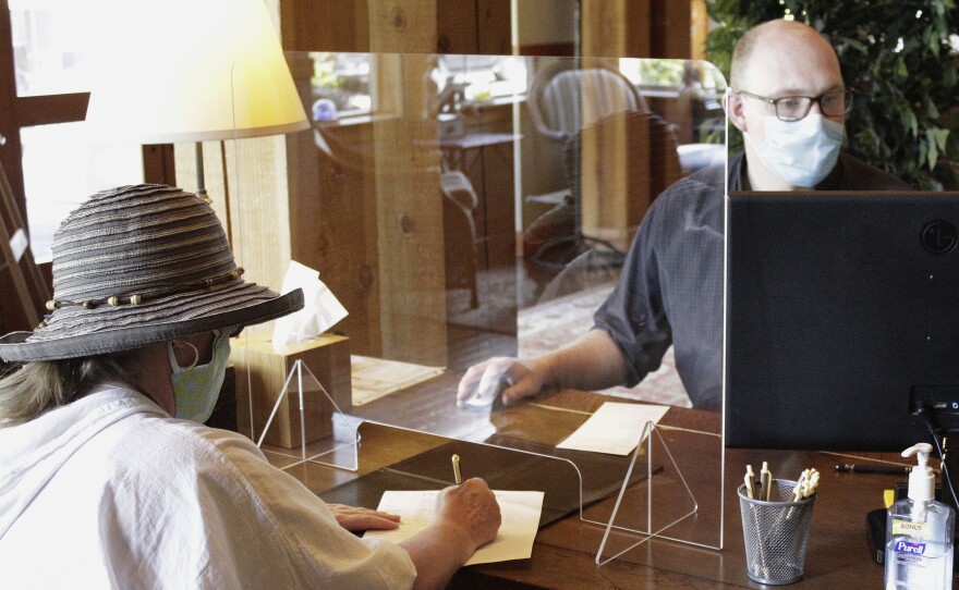 A hotel employee helps a guest from behind protective plastic last month at the Ocean Lodge in Cannon Beach, Ore.