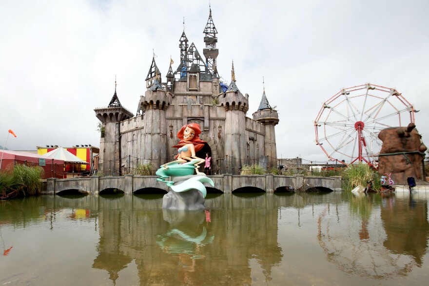 A glitched Little Mermaid piece sits in front of a dismal castle as part of the artist Banksy's biggest show to date, titled <em>Dismaland,</em> at Tropicana in Weston-super-Mare, England.