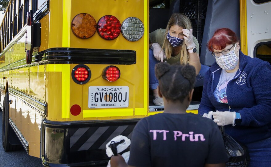 Teachers, Jennifer Scandle, left, and Renee Roberts, right, hand out a lunch to Kelsi Clarke, center, from a school bus.