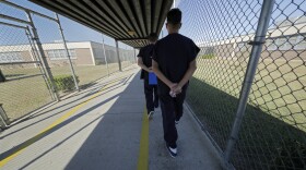 Detainees walk with their hands clasped behind their backs along a line painted on a walkway inside the Winn Correctional Center in Winnfield, La.