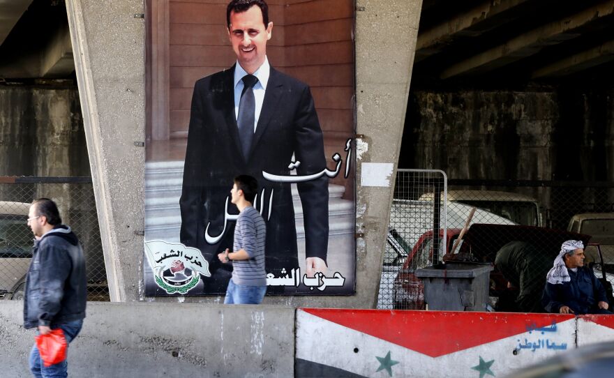 Syrian men walk past a poster bearing a portrait of President Bashar Assad in Damascus, on Feb. 27, 2016.
