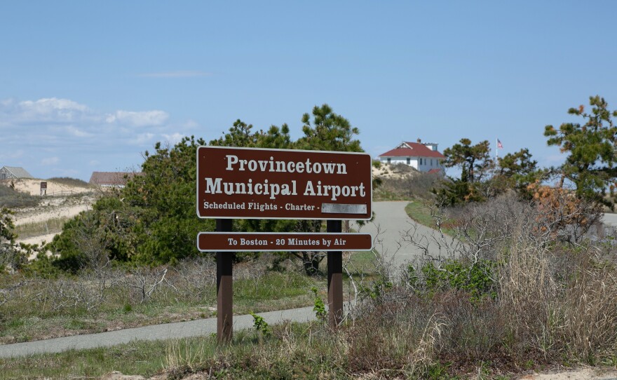 The sign for the Provincetown Municipal Airport with the National Park Service Race Point Beach ranger station in the distance.