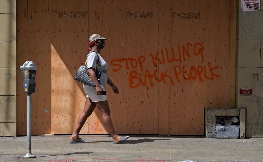 A woman walks past a boarded up store in downtown Los Angeles on Sunday. Professor Jody David Armour says protesters today are more diverse and have more empathy than in 1992.
